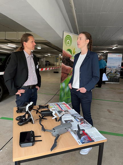 Vergrößerung des Bildes für Tobias Bräunig, Präventionsfachmann der SVLFG und Bianca Grütze vom Fraunhofer- Institut stehen vor einem Tisch auf der eine Drohne steht. Die beiden befinden sich im Gespräch..