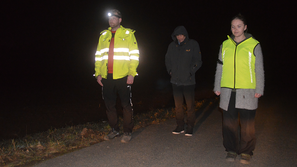 Vergrößerung des Bildes für Zwei Menschen tragen in der Dunkelheit eine Warnweste, einer nicht..