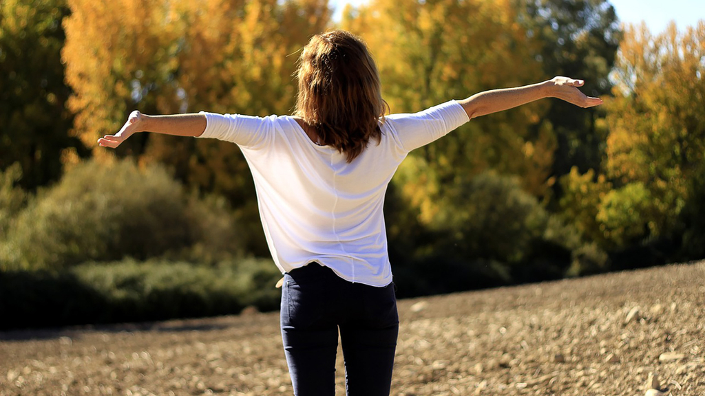 Vergrößerung des Bildes für Eine Frau steht auf einem Feld und streckt ihre Arme aus und atmet tief durch.