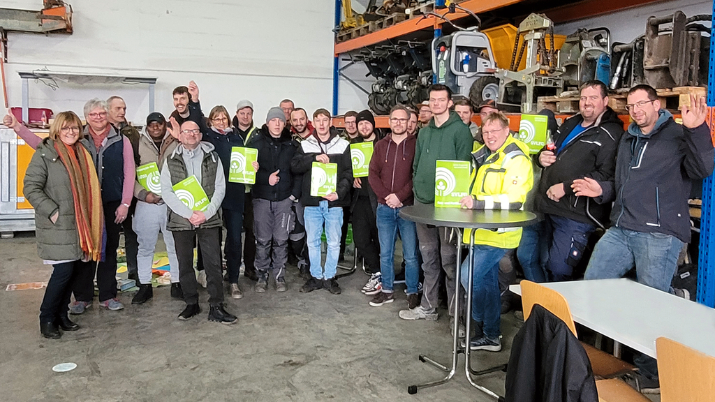 Vergrößerung des Bildes für Gruppenfoto der Teilnehmenden des Ernährungsworkshops in der Maschinenhalle des Betriebs.