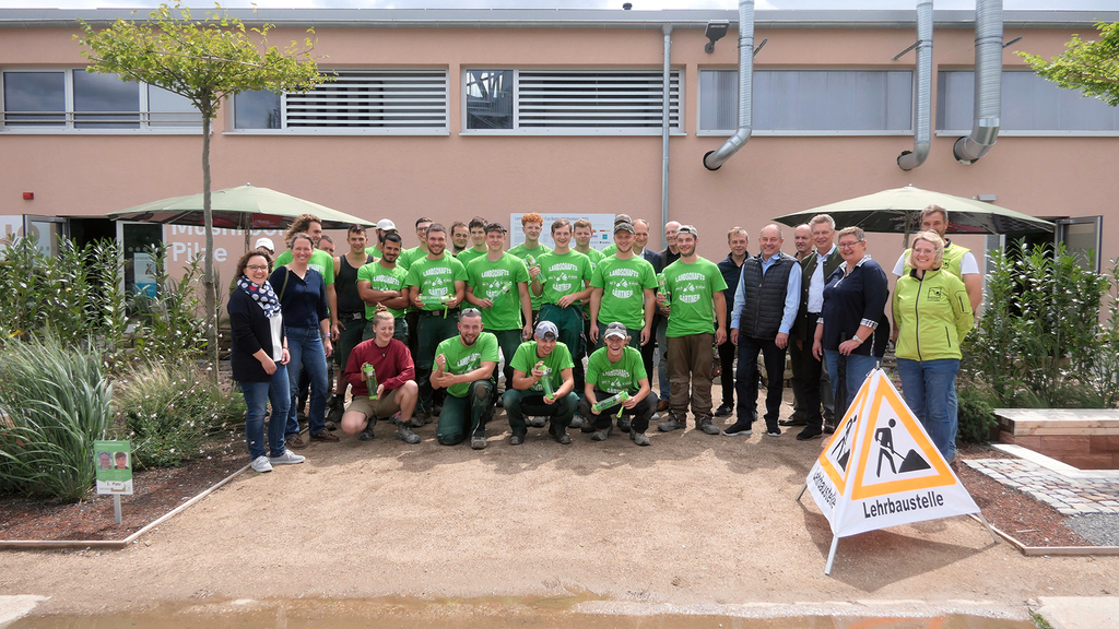 Vergrößerung des Bildes für Azubis und Personen der SVLFG stehen zusammen auf der Lehrbaustelle und präsentieren die Trinkflaschen.