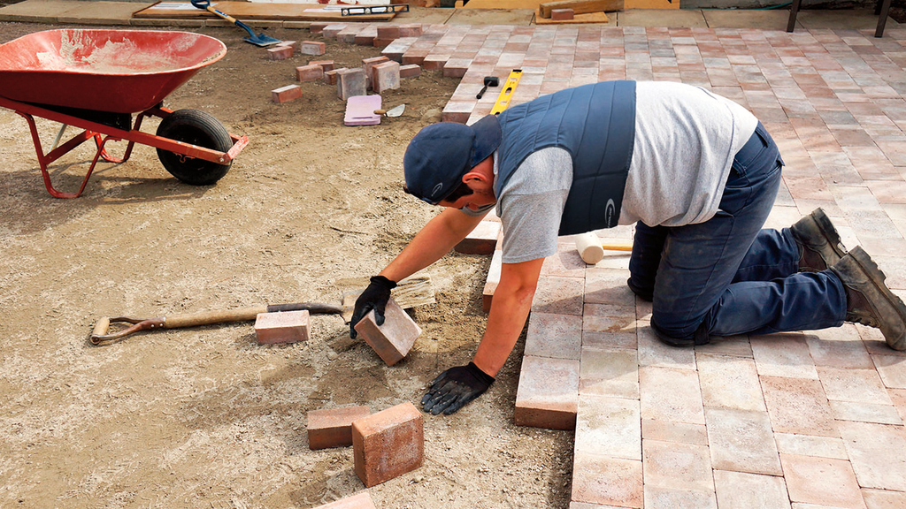 Vergrößerung des Bildes für Arbeiter beim legen von Pflastersteinen. Er trägt Kühlkleidung.  .