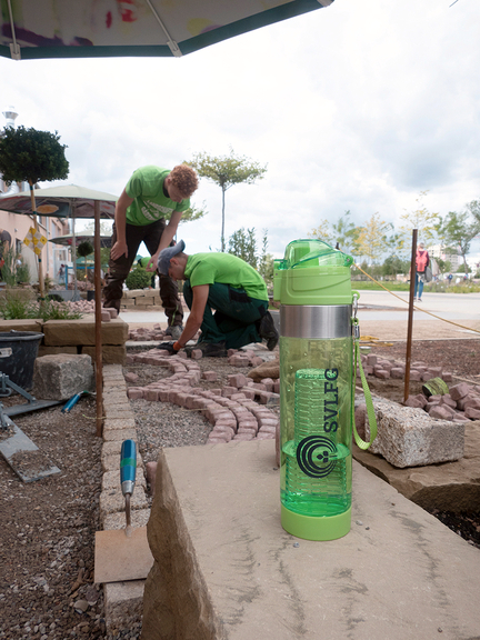 Vergrößerung des Bildes für Zwei junge Männer arbeiten auf der Baustelle. Im Fokus steht eine Trinkflasche..