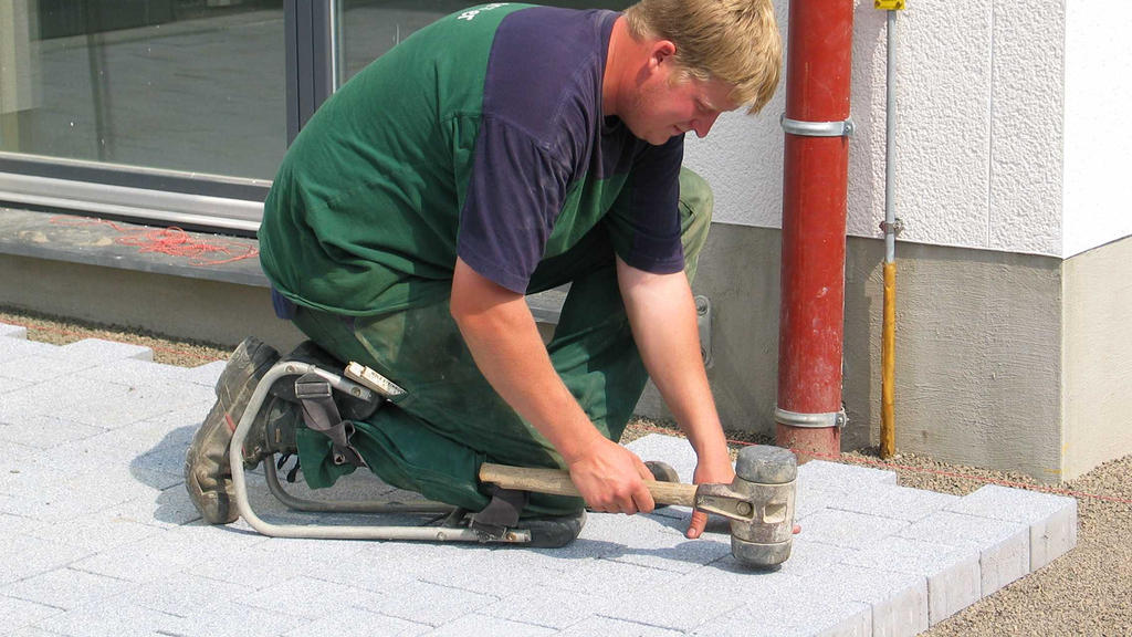 Vergrößerung des Bildes für Ein Mann mit Kniehilfe pflastert den Boden.