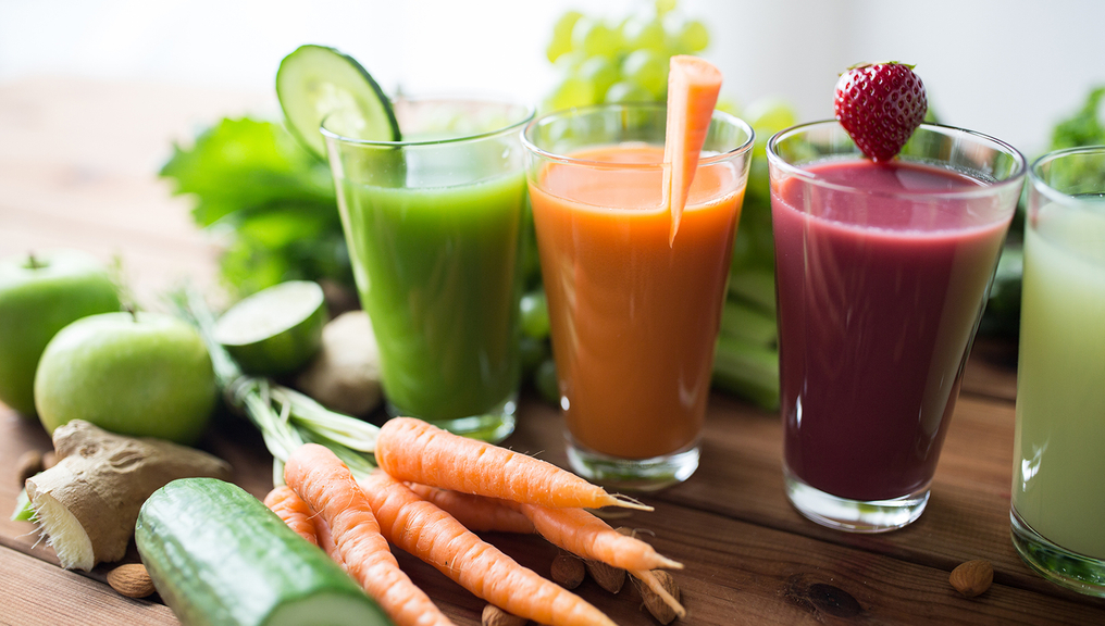 Vergrößerung des Bildes für Drei Gläser mit Smoothies in grün, orange und dunkelrot. Daneben liegen zwei Äpfel, eine angeschnitte Gurke und eine Möhre..