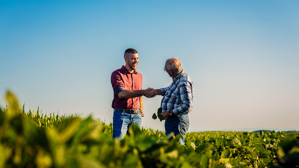 Vergrößerung des Bildes für Ein Mann gibt einem anderen Mann die Hand auf einem Feld.