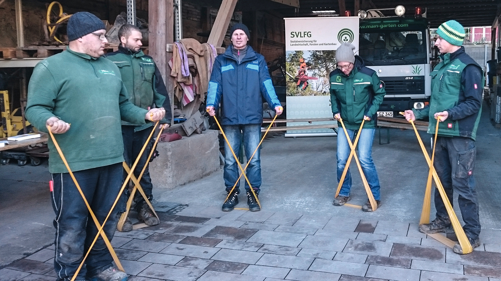 Vergrößerung des Bildes für Männer führen im Stehen eine Rückenübung mit dem Theraband aus.