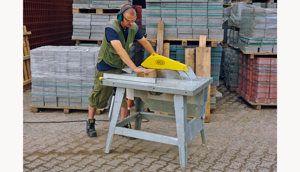 Vergrößerung des Bildes für Arbeiter in Schutzkleidung und Gehörschutz an einer Tischkreissäge mit Schutzvorrichtungen.