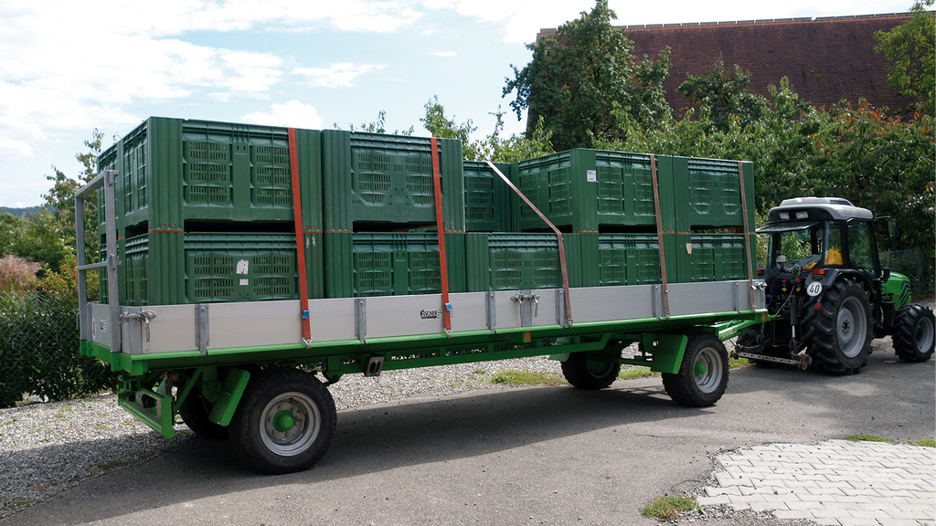 Vergrößerung des Bildes für Ein Anhänger am Traktor hat Obstkisten zweistöckig geladen. Die Ladung ist mit Spanngurten richtig gesichert..