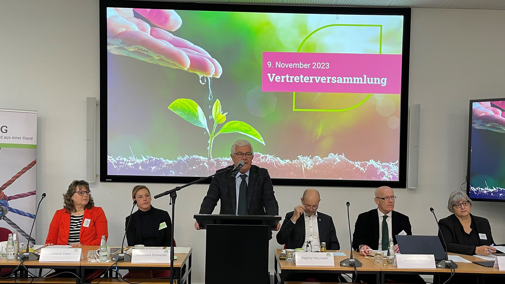 Vergrößerung des Bildes für Der Vorstandsvorsitzender steht an einem Rednerpult vor einem Whiteboard. Hinter ihm sitzen fünf andere Personen an Tischen..