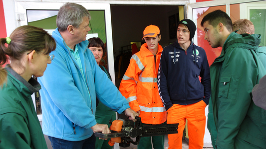 Mann zeigt jungen Menschen die Funktionsweise einer elektrischen Heckenschere