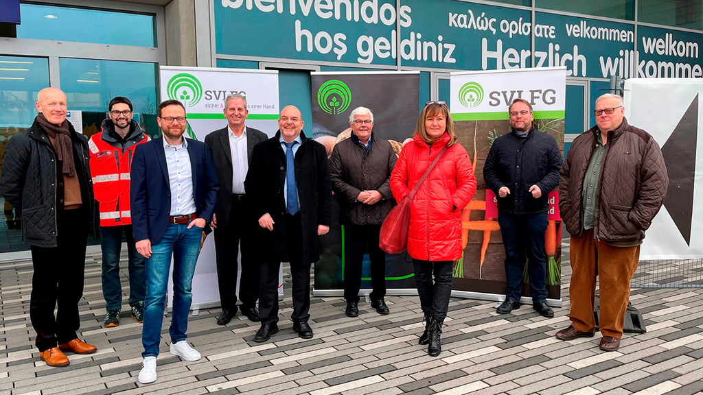 Vergrößerung des Bildes für Eine Gruppe steht vor drei Roll-ups mit dem Logo der SVLFG und einem Gebäude mit der Begrüßung "Herzlich willkommen" in mehreren Sprachen..