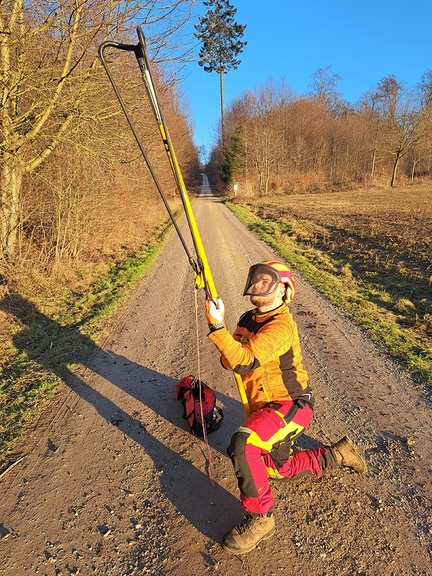Vergrößerung des Bildes für Mann wendet den Wurfbeutelschleuder an. Er kniet auf einem Feldweg, Er trägt Personenschutzkleidung..