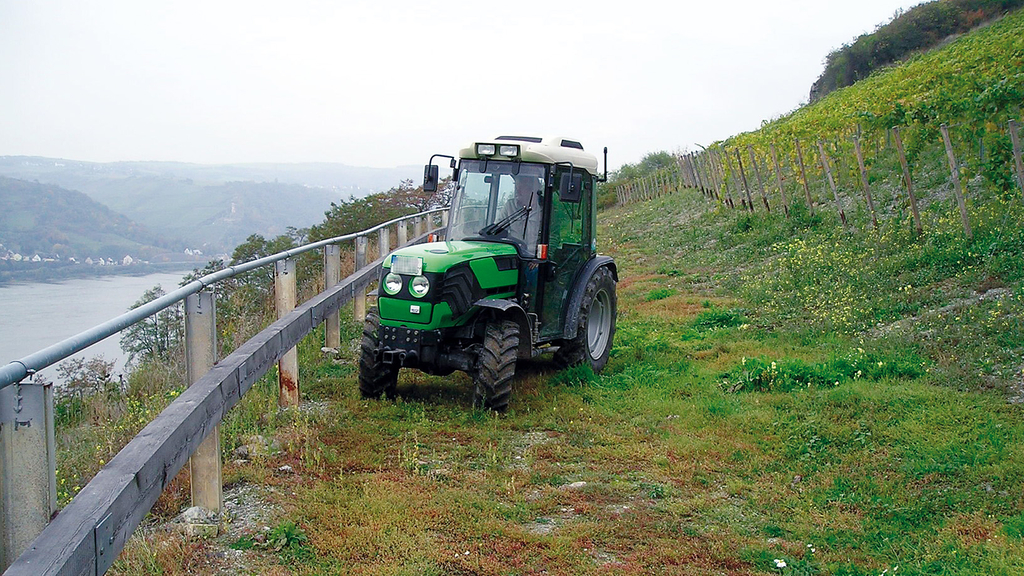 Vergrößerung des Bildes für Ein Schmalspurtraktor wendet am unteren Ende des Steilhangs mit Weinreben nahe am Geländer, das zum dahinterliegenden Fluss hin abgrenzt und schützt..