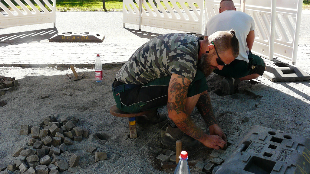 Vergrößerung des Bildes für Mann sitzt auf kleinem Hocker beim Verlegen von Pflastersteinen.