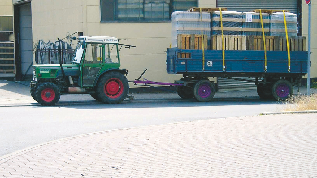 Vergrößerung des Bildes für Auf dem Bild befindet sich ein Traktor mit Anhänger. Der Anhänger hat Paletten und leere Flaschen geladen. Die Ladung ist mit Spanngurten gesichert. .