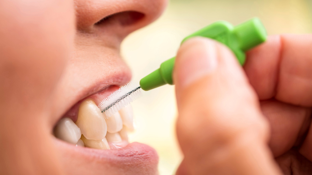 Vergrößerung des Bildes für Person reinigt sich mit Zahnzwischenraumbürste die Zähne..