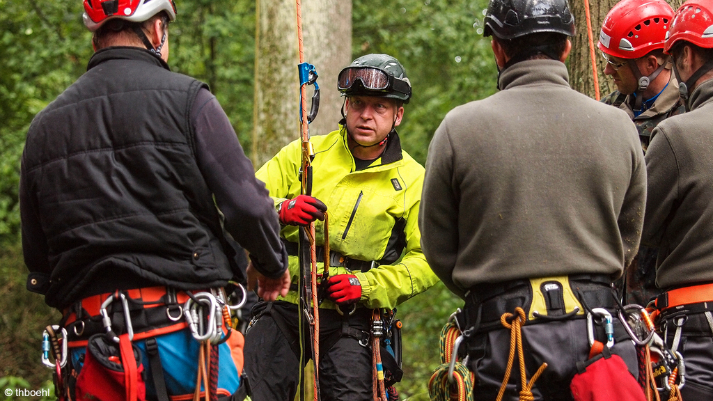 Vergrößerung des Bildes für Männer im Wald mit Seilkletterausrüstung ausgestattet bei einer Besprechung.
